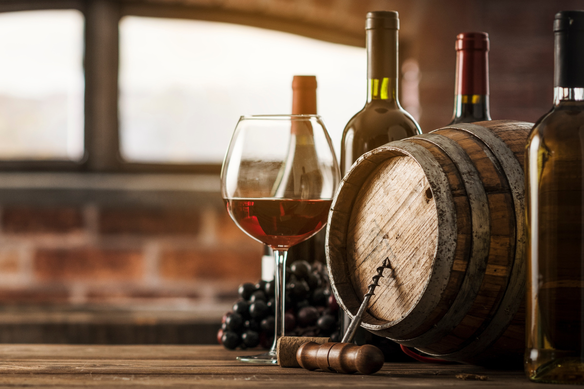 Glas Rotwein neben Mehrwegflaschen und Holzfass